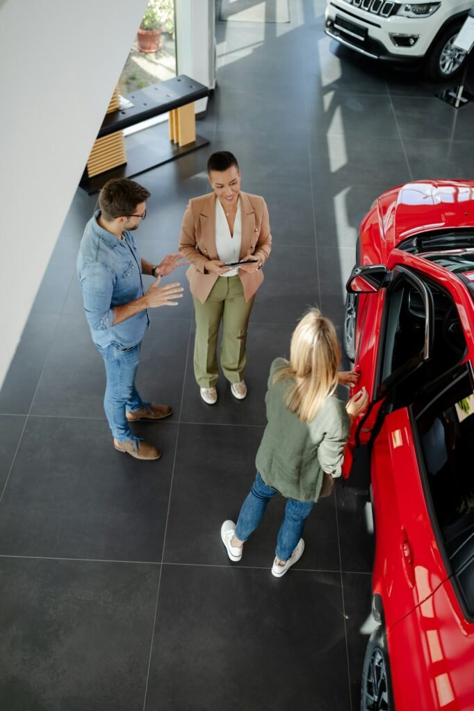 Woman is opening a door,trying a new car while man and saleswoman discussing about car performances.